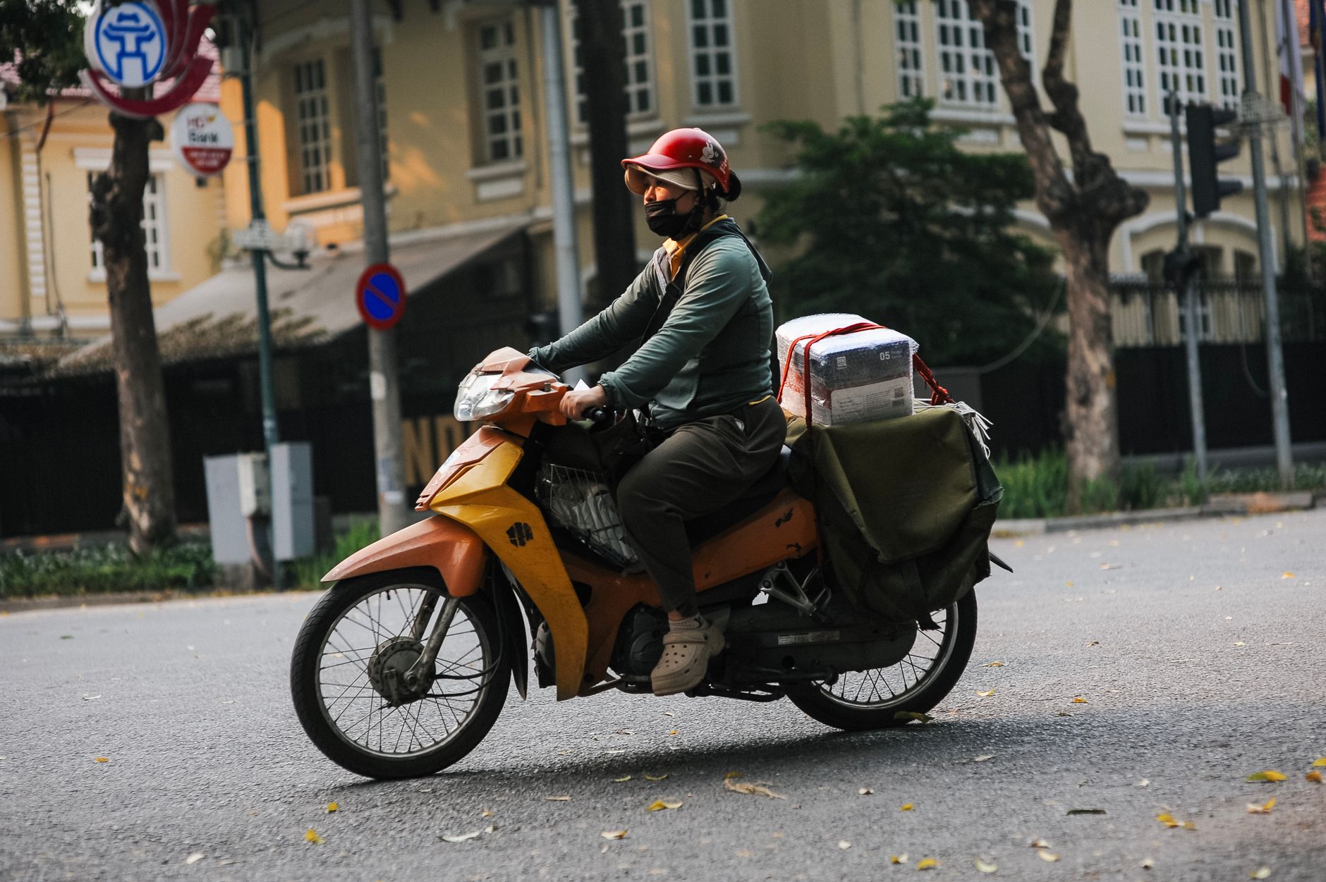 Entregador em uma scooter com bagageiro trafegando por rua arborizada